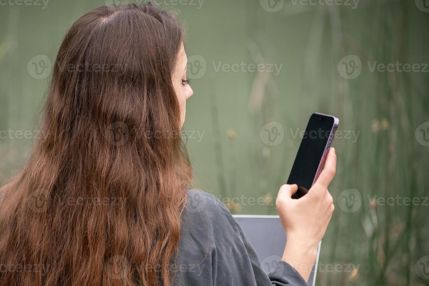 A woman is sitting on a dock with a laptop and a cell phone. She is talking on the cell phone while using the laptop. photo
