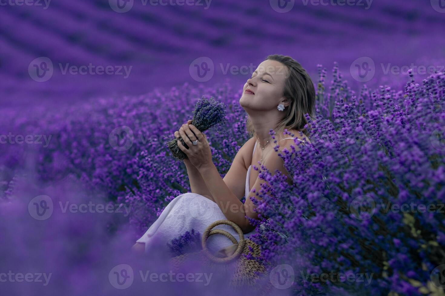 A woman sits in a field of lavender flowers, holding a bunch of lavender in her hand. She is enjoying the scent and the peaceful atmosphere of the field. photo
