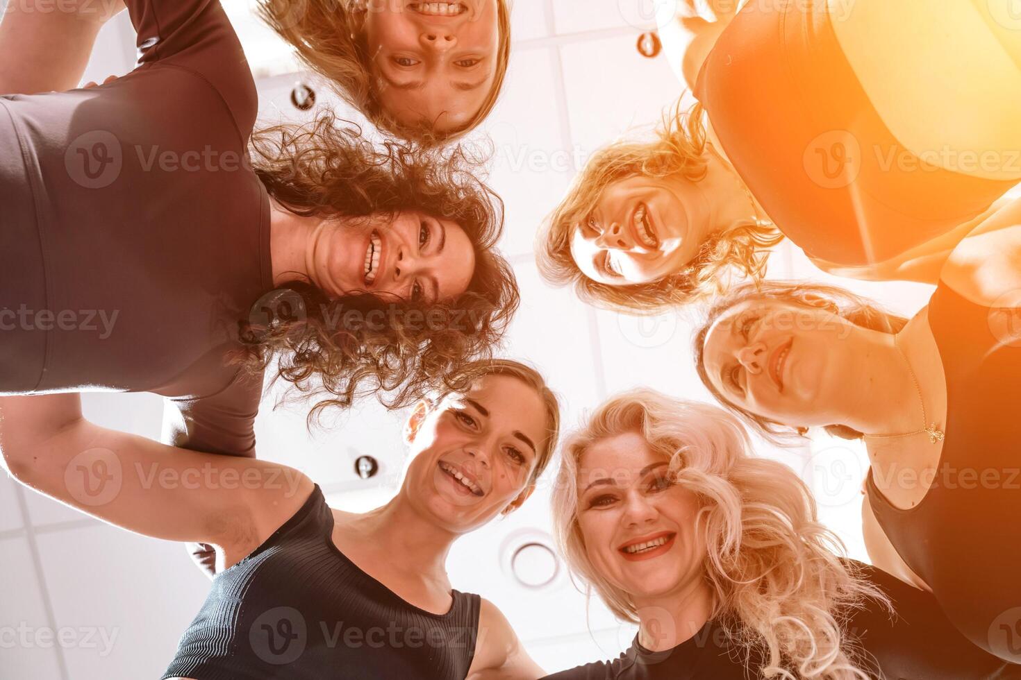 Low angle shot of smiling women looking at the camera, hugging, standing in a circle and doing team building photo