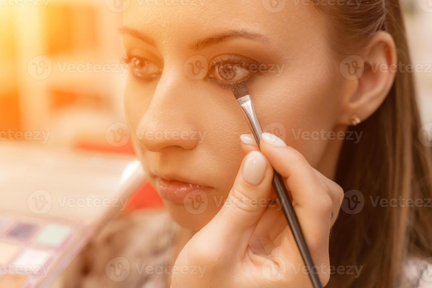 Make-up artist working with brush on model eyes Close up of applying make up on young girl,semi profile, professional make up in beauty studio photo