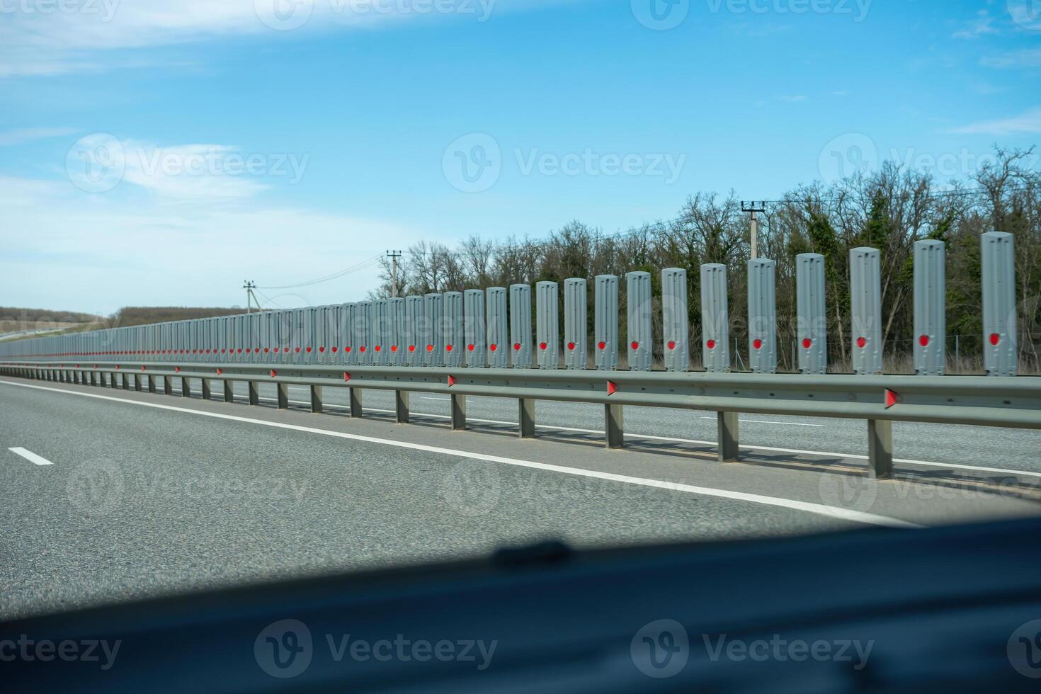 A road with a long line of metal posts with red hearts on them. The road is empty and the sky is clear. photo