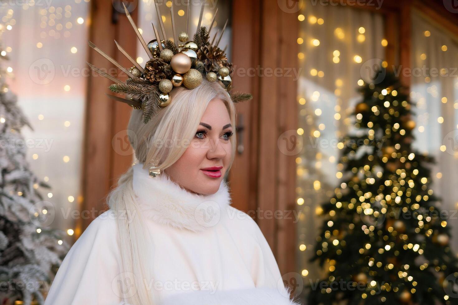 Happy blonde as Snow Maiden in white costume. Wooden house exterior Festive setting. Character with crown creating festive scene. photo