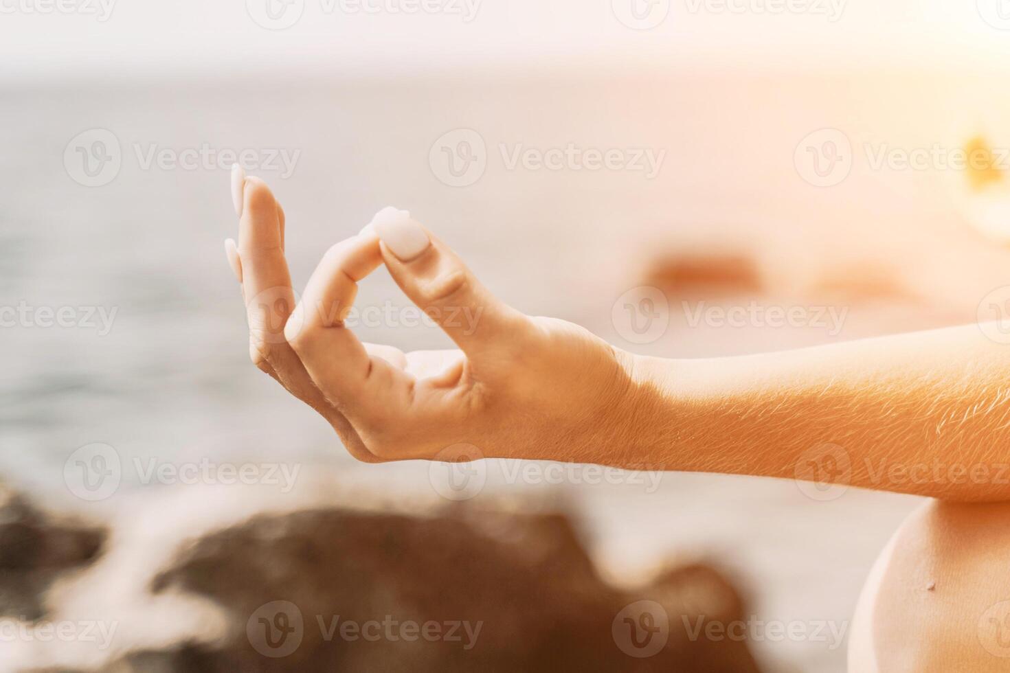 Yoga on the beach. A happy woman meditating in a yoga pose on the beach, surrounded by the ocean and rock mountains, promoting a healthy lifestyle outdoors in nature, and inspiring fitness concept. photo