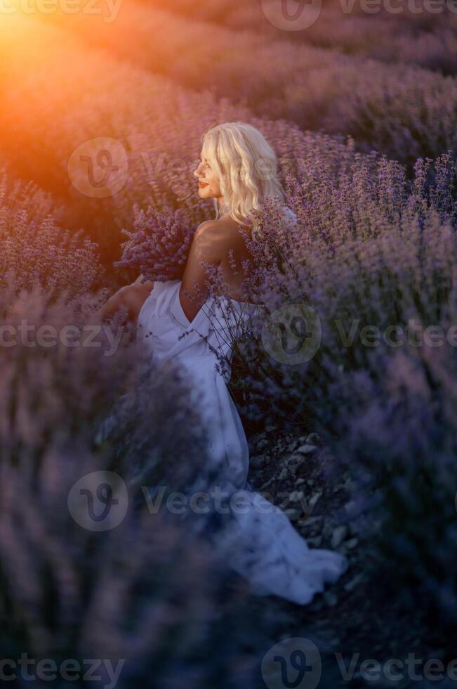 rubia mujer poses en lavanda campo a puesta de sol. contento mujer en blanco vestir sostiene lavanda ramo. aromaterapia concepto, lavanda aceite, foto sesión en lavanda