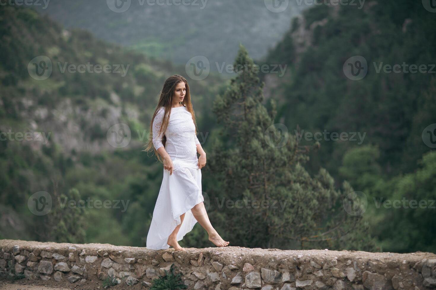 A woman in a white dress is walking on a stone wall photo