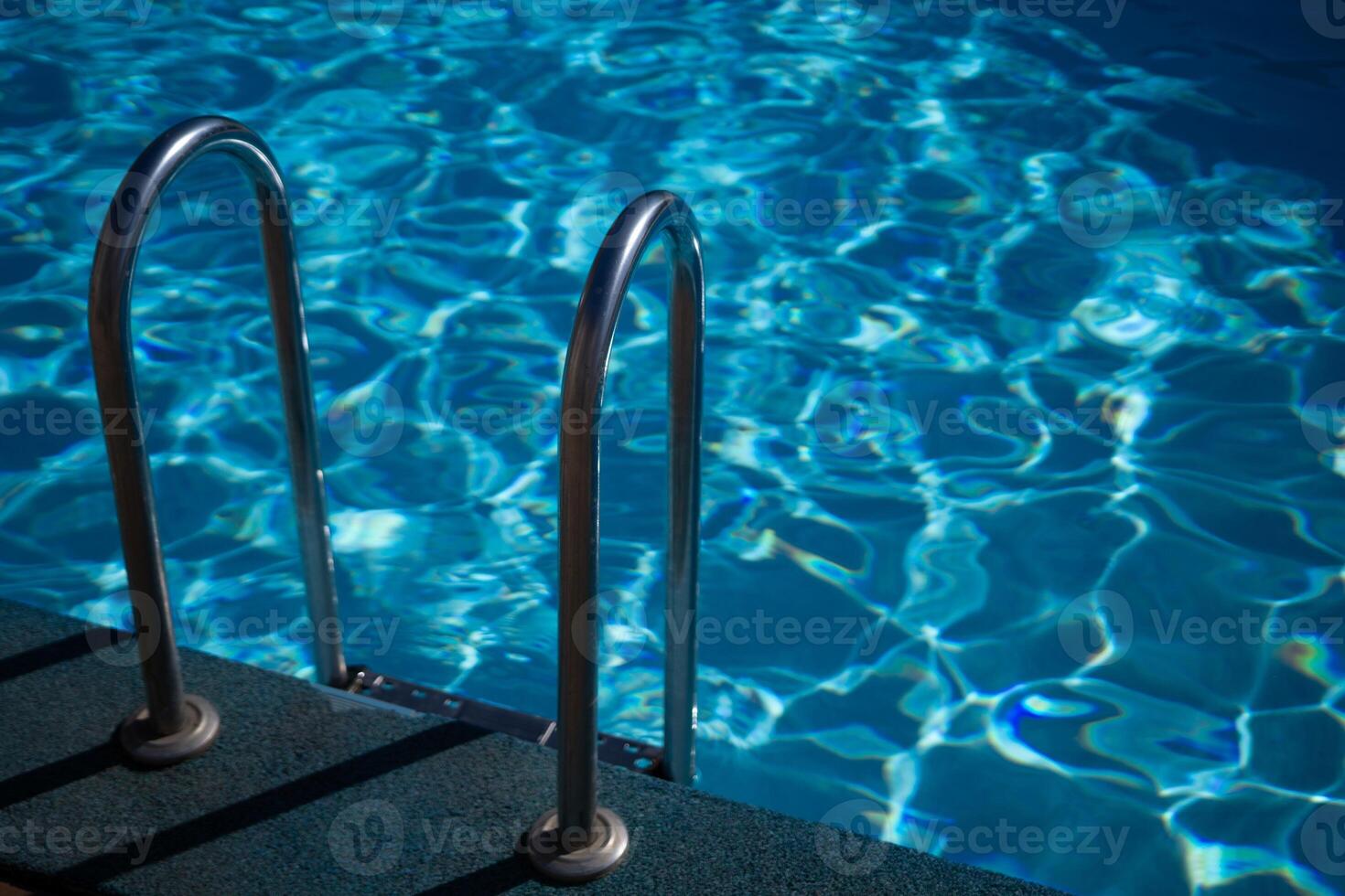 A metal ladder is in the water. The water is clear and calm. The ladder is in the middle of the pool. photo