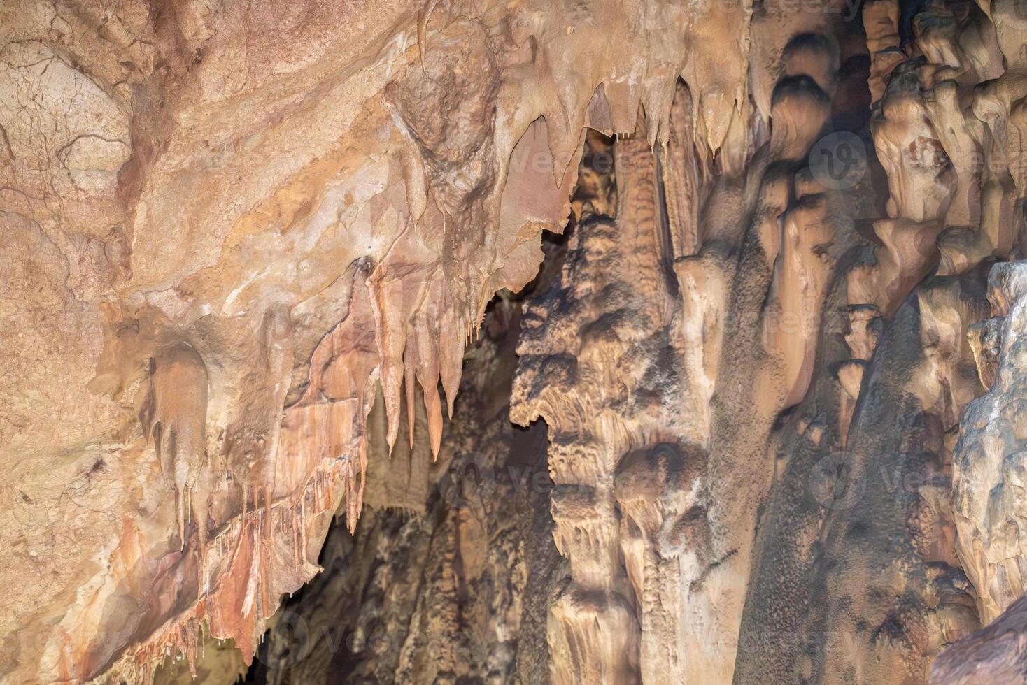A cave with a lot of rock formations and stalactites hanging from the ceiling. Scene is mysterious and awe inspiring. photo