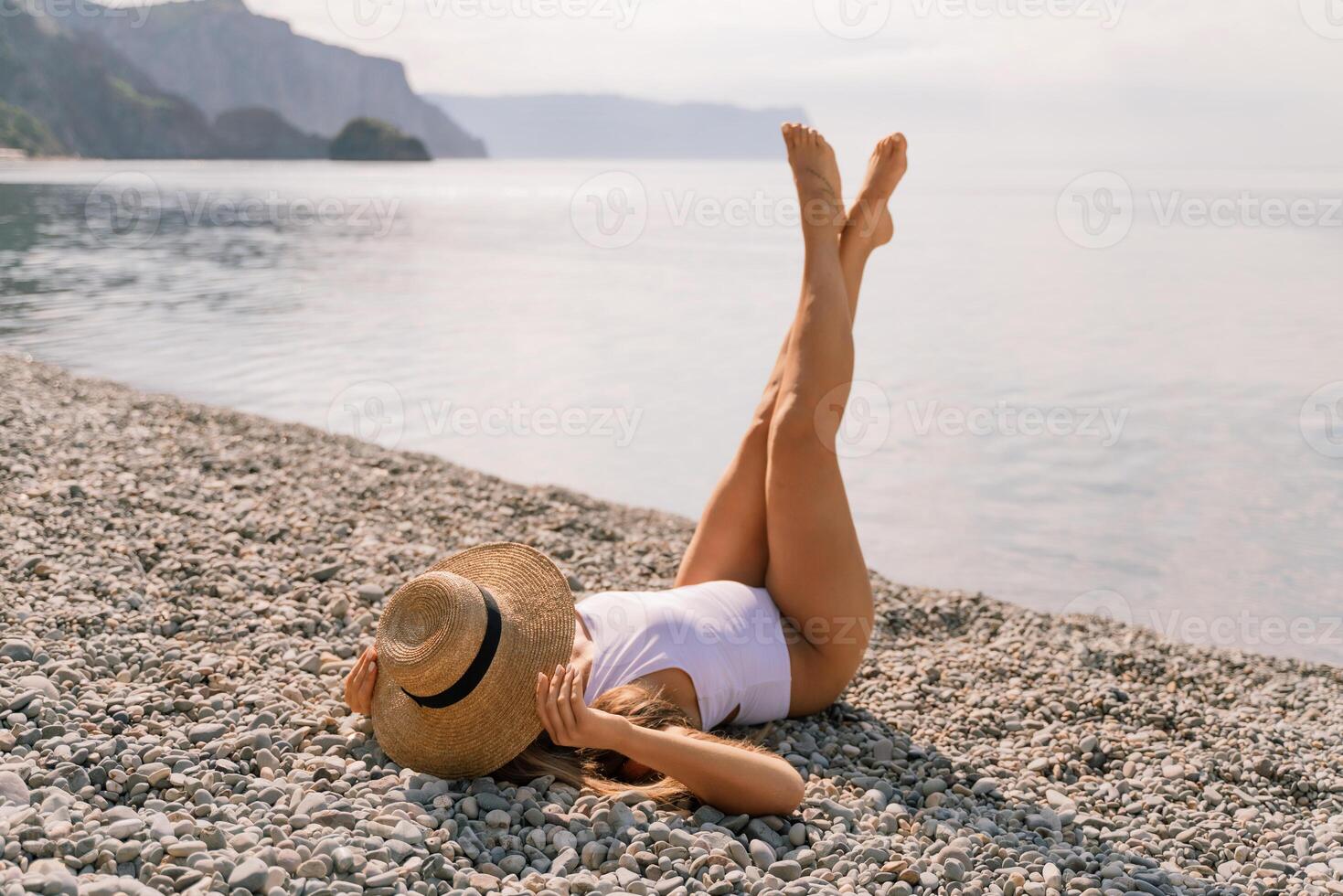 A woman is laying on the beach wearing a straw hat and a white bikini. She is enjoying the sun and the beach. photo