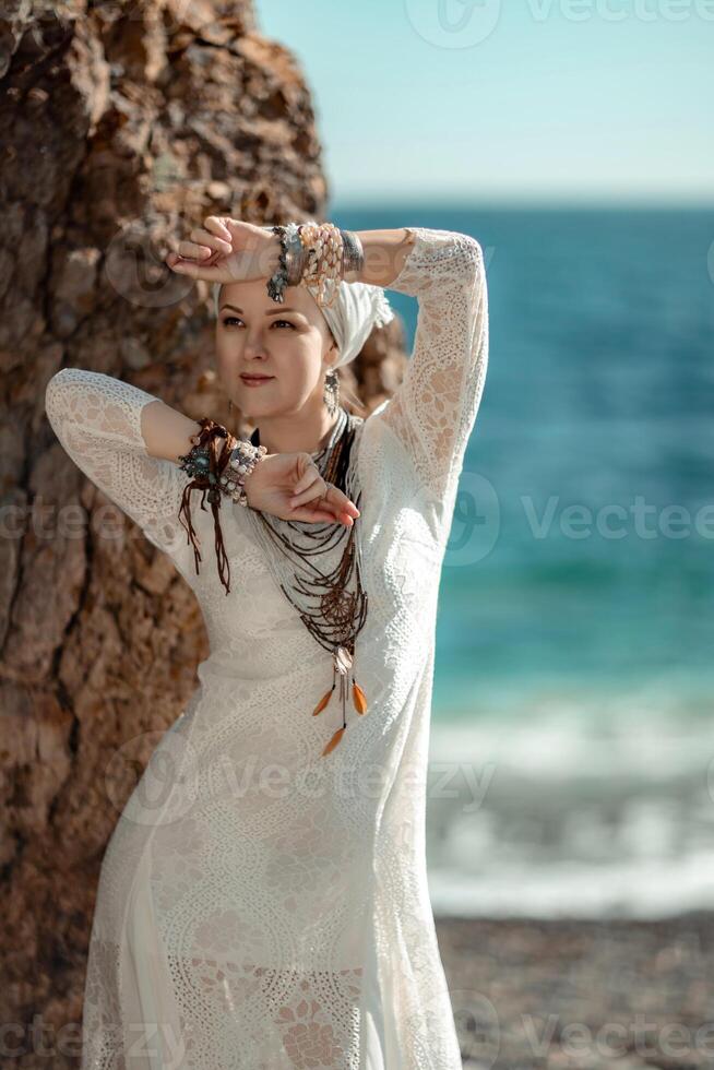 Middle aged woman looks good with blond hair, boho style in white long dress on the beach decorations on her neck and arms. photo