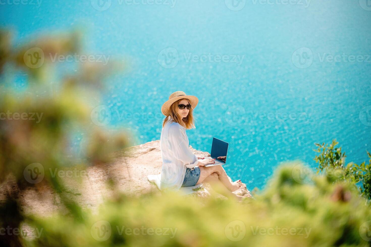Freelance woman working on a laptop by the sea, typing away on the keyboard while enjoying the beautiful view, highlighting the idea of remote work. photo