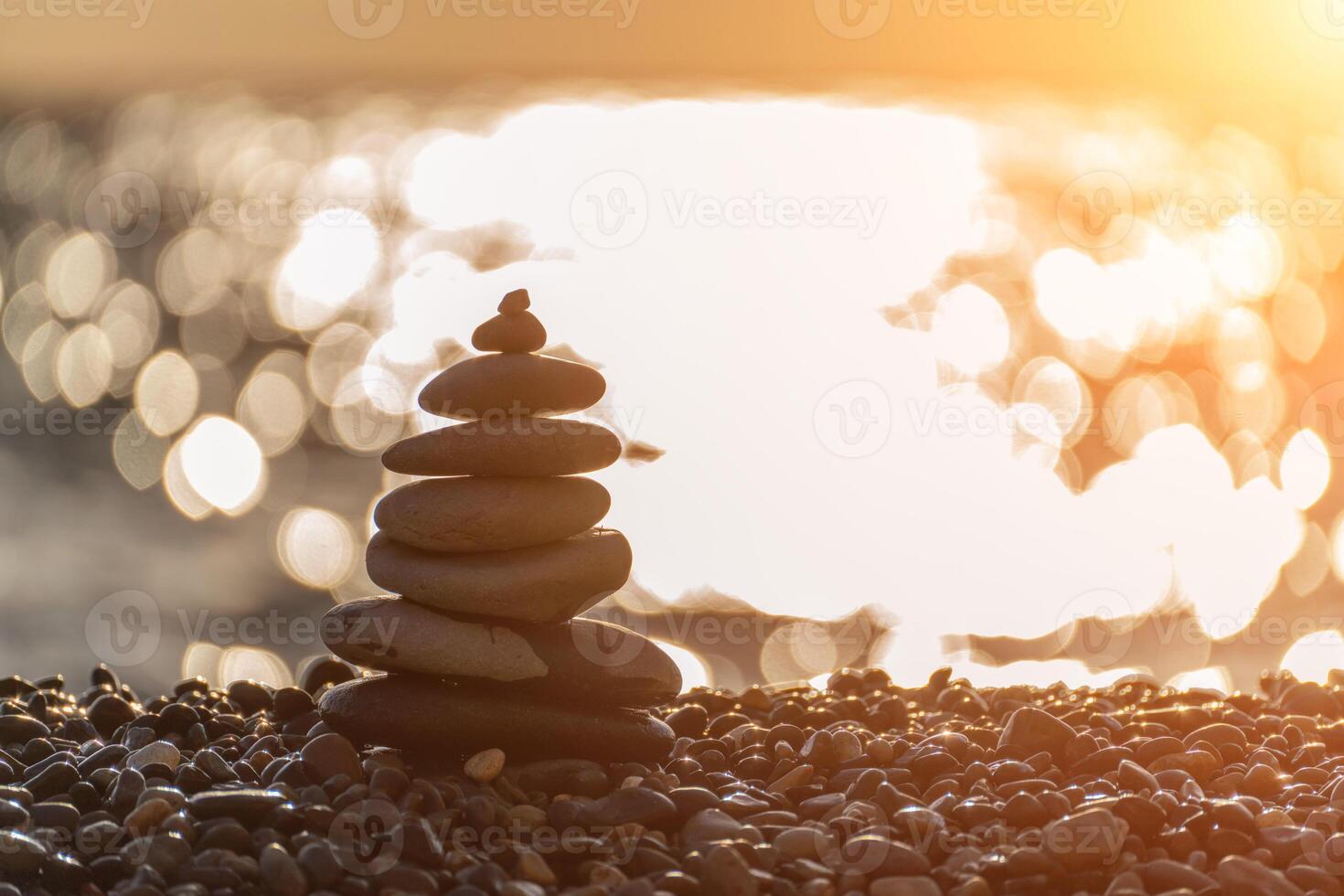 Balanced rock pyramid on pebbles beach. Golden sea bokeh on background. Selective focus, zen stones on sea beach, meditation, spa, harmony, calm, balance concept. photo