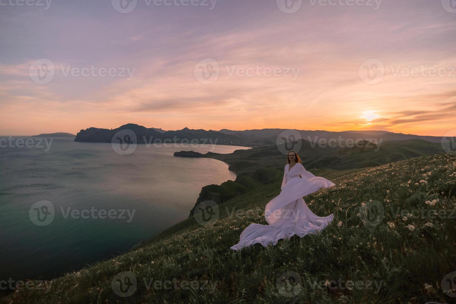 A woman in a white dress is standing on a hill overlooking the ocean photo