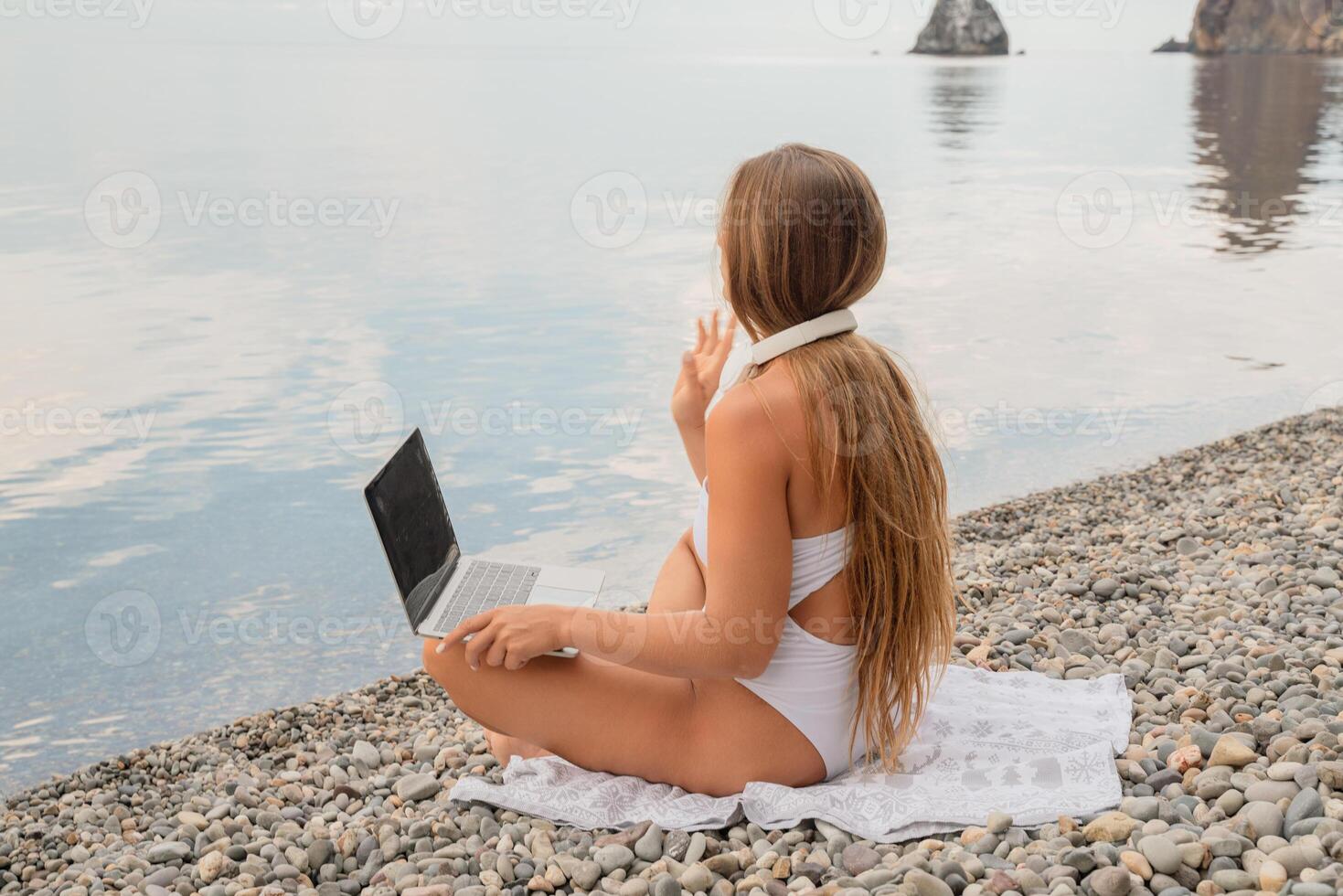 A woman is sitting on the beach with a laptop open in front of her photo
