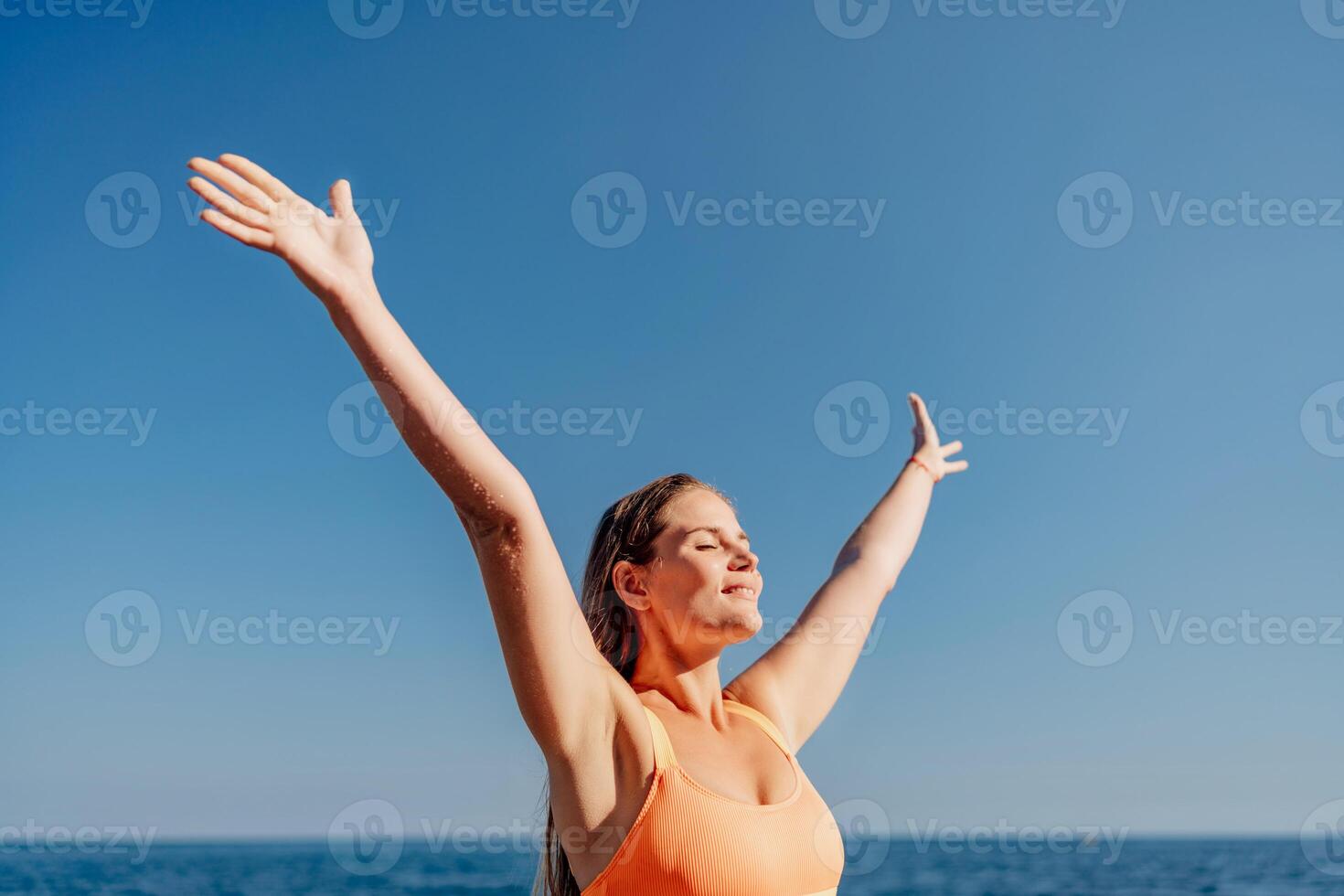 A woman is standing on the beach with her arms raised in the air, smiling photo