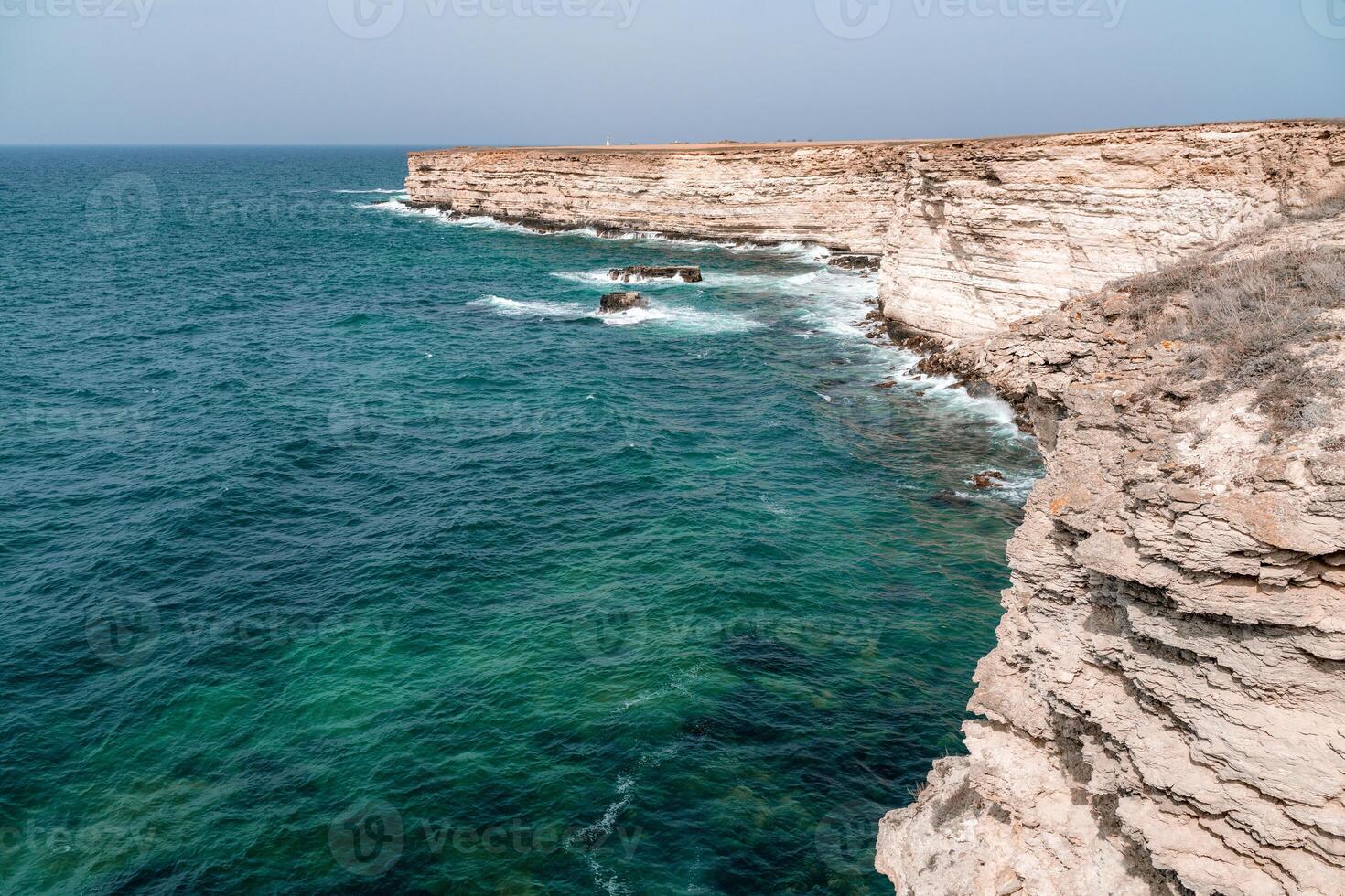 The ocean is calm and the shoreline is rocky. The water is a deep blue color. The rocks are jagged and the waves are small. The scene is peaceful and serene. photo