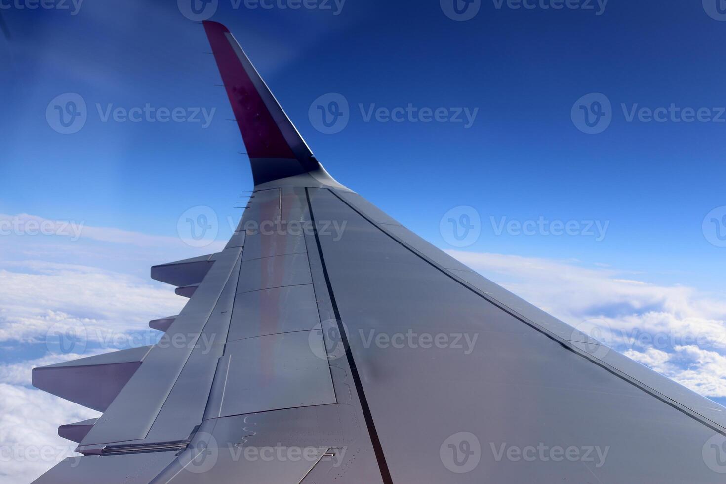 The wing of a jet plane and the scenery on the ground are visible through the porthole. photo