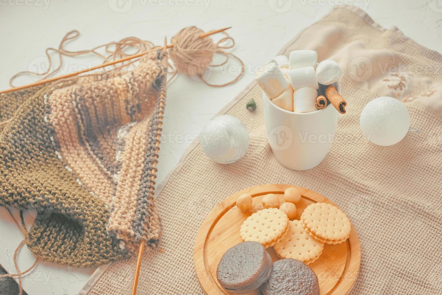Hot drink with marshmallows and a tube of cinnamon. cookies with Christmas needles. unfinished scarf with knitting needles photo
