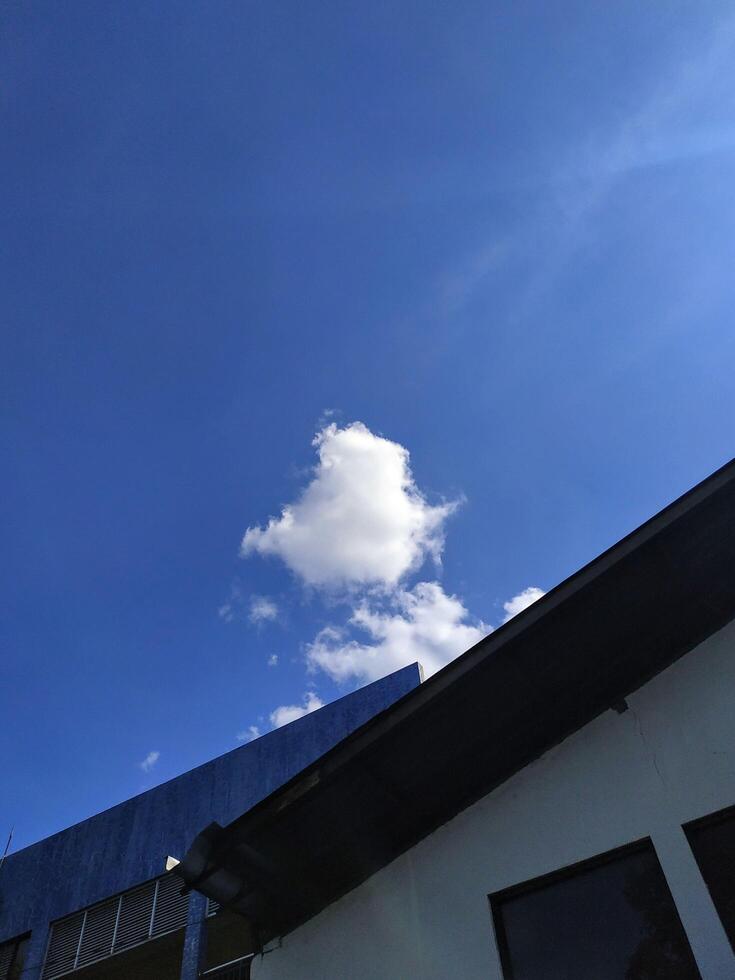 white clouds in the blue sky with roofs of buildings below photo