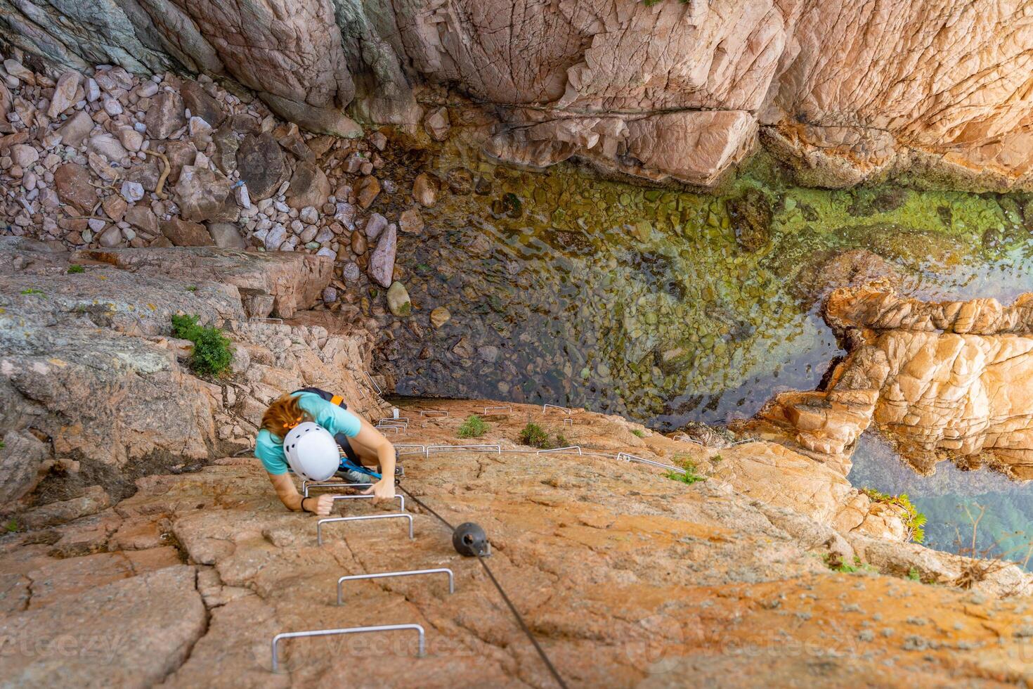 Pretty female climber strong success hiking on rocks over the sea with rope and helmet. photo