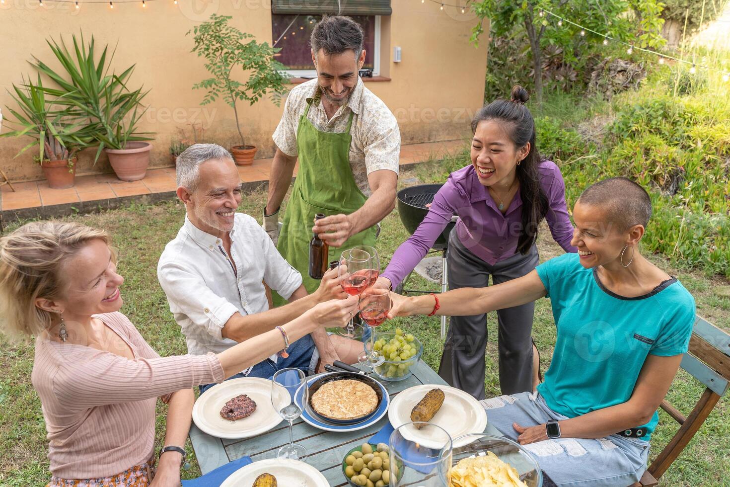 Multiracial family toasting with big smile around the table at house patio diner. photo