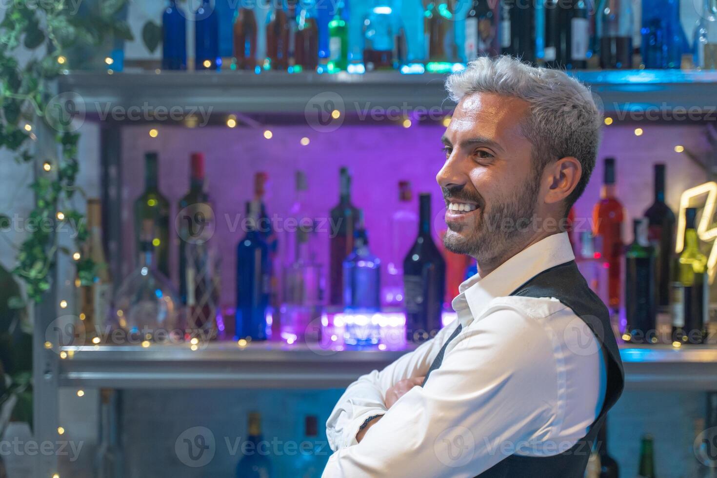 Barman portrait in a white shirt and black apron smiling at nightclub. photo