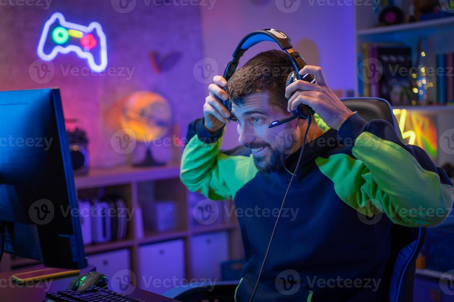 Gamer playing excited online game with headphones streaming on computer in a neon light room. photo