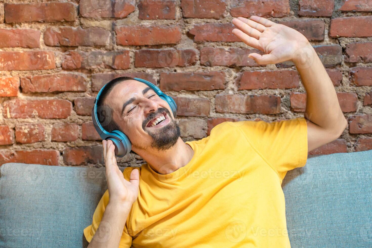 Portrait of young handsome man listening to music with headphones against brick wall photo