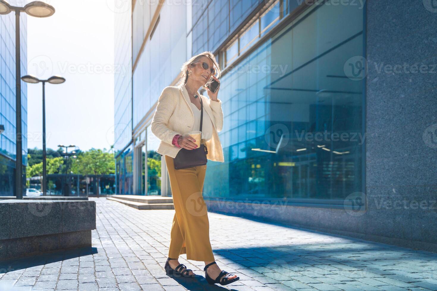 Happy attractive businesswoman talking with her smart phone in front of a modern building. photo