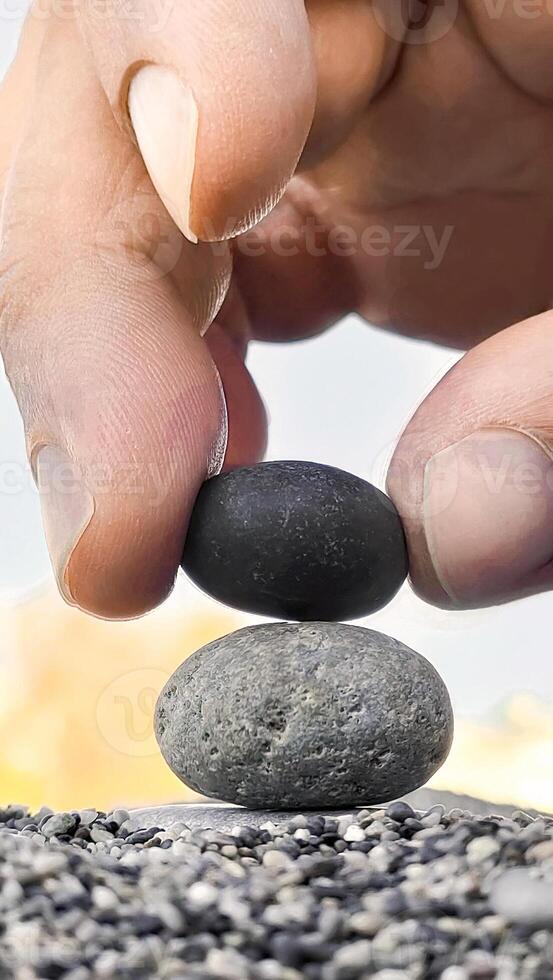 Hand of man places black stone on gray stone creating a pyramid, zen concept, vertical frame. photo