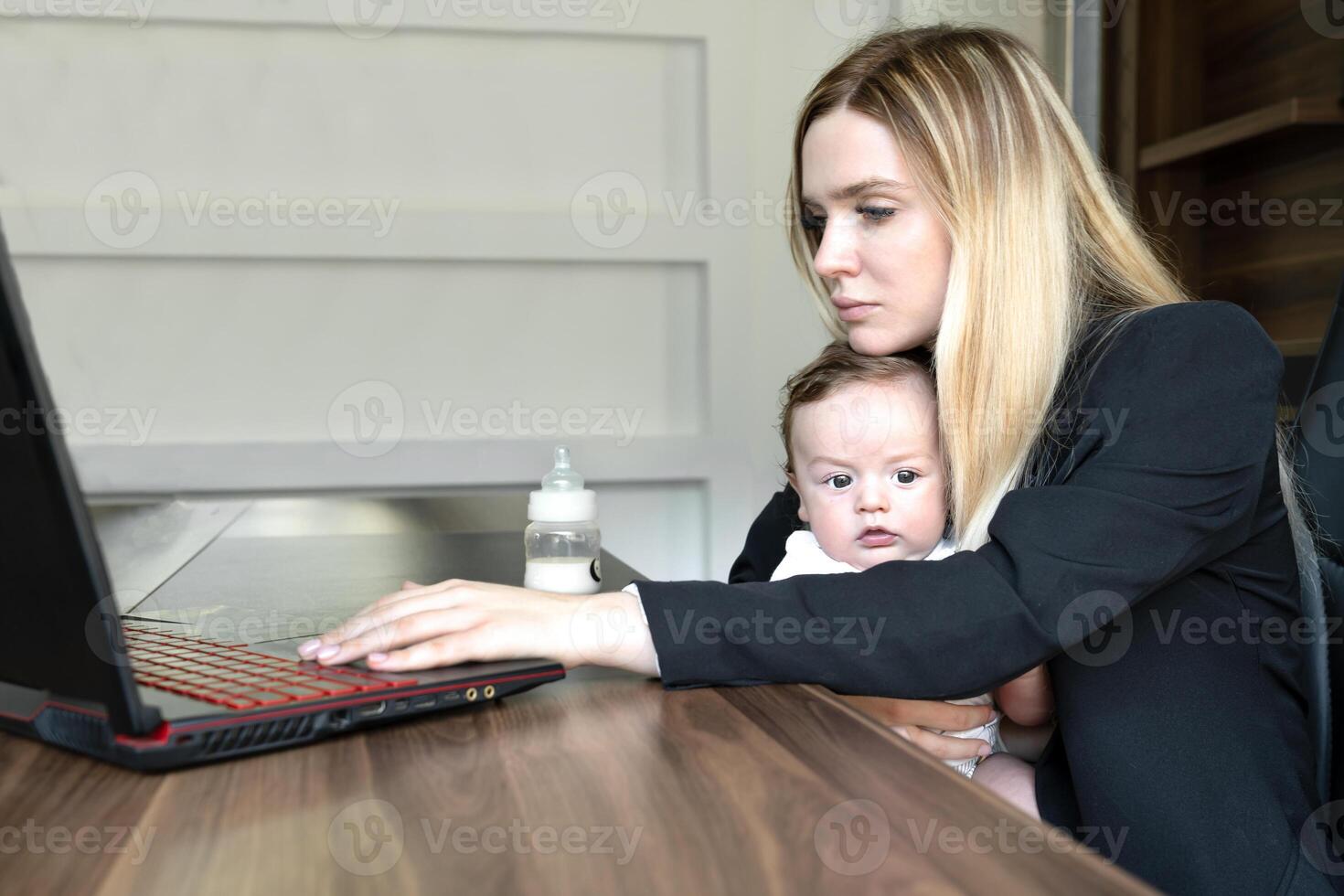 Young woman holds baby in her arms, in office, combining this with working on laptop., concept of combining business and caring for newborn baby photo