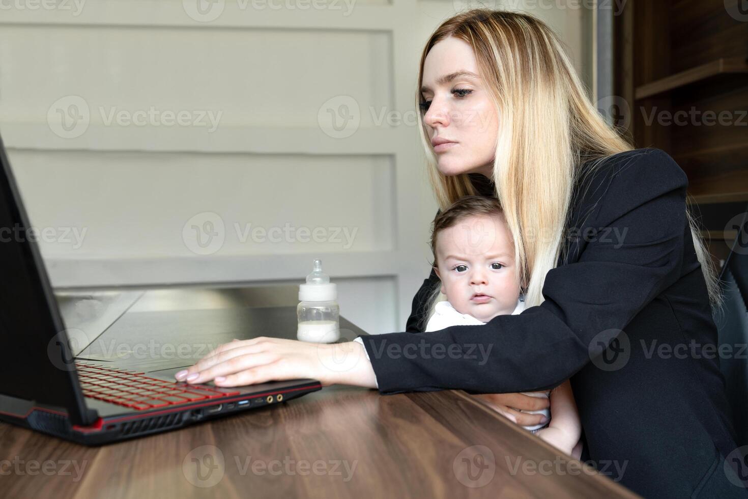 Concept of combining business and caring for newborn baby. young businesswoman holds baby in her arms, in office, combining this with working on laptop. photo