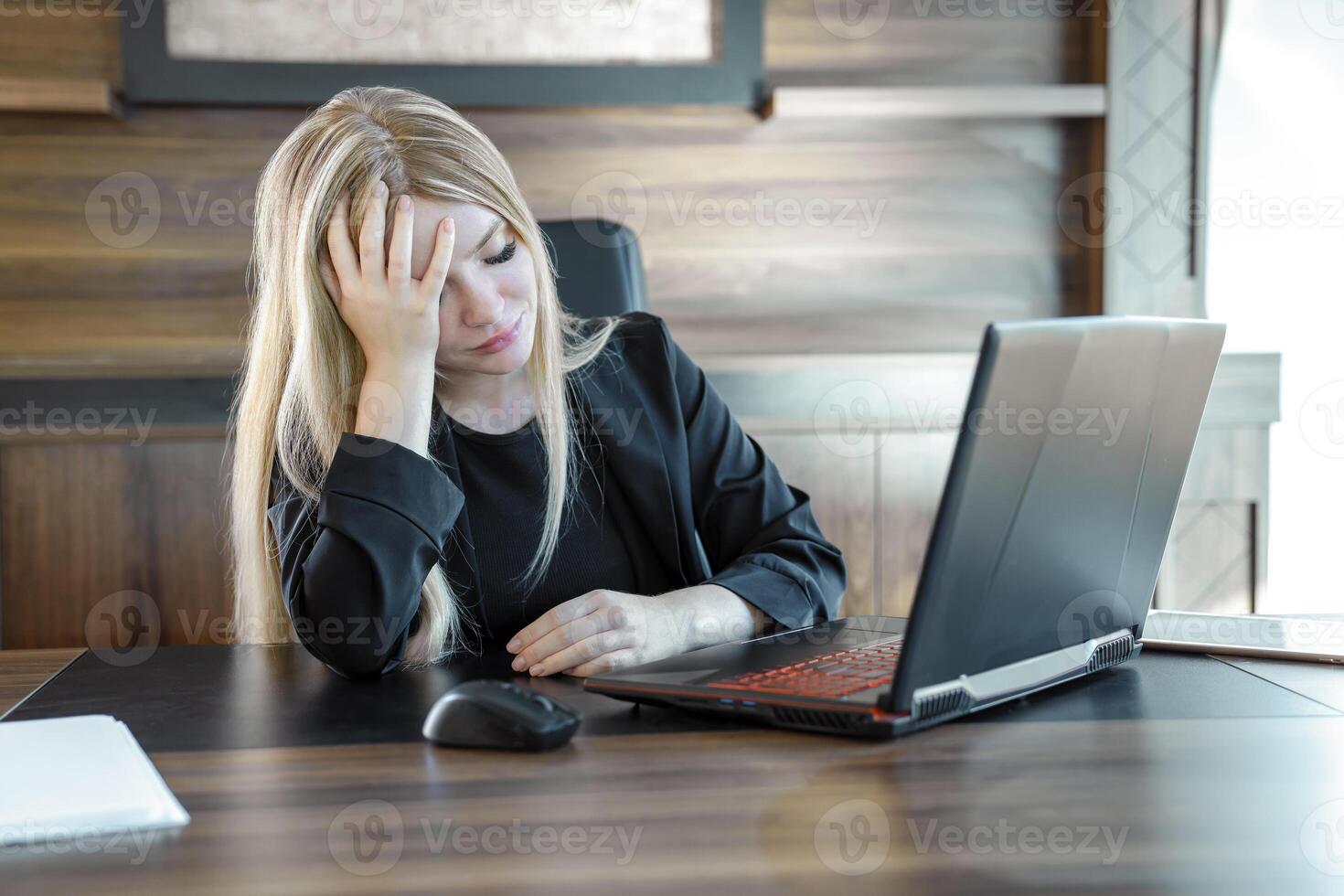 Distressed young business woman in black suit is sitting with eyes closed in front of laptop in office. photo