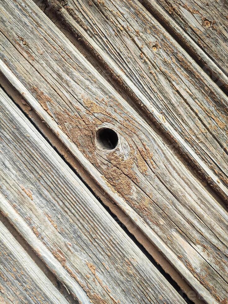 Texture of a wooden plank fence with diagonal wood strips and a hole in the center, gray brown wooden wall texture photo