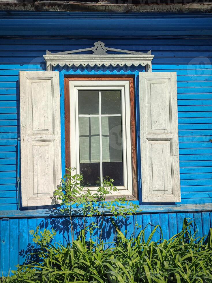 Window of an old blue wooden village house with open white shutters and greenery on sunny day, bright building backdrop photo