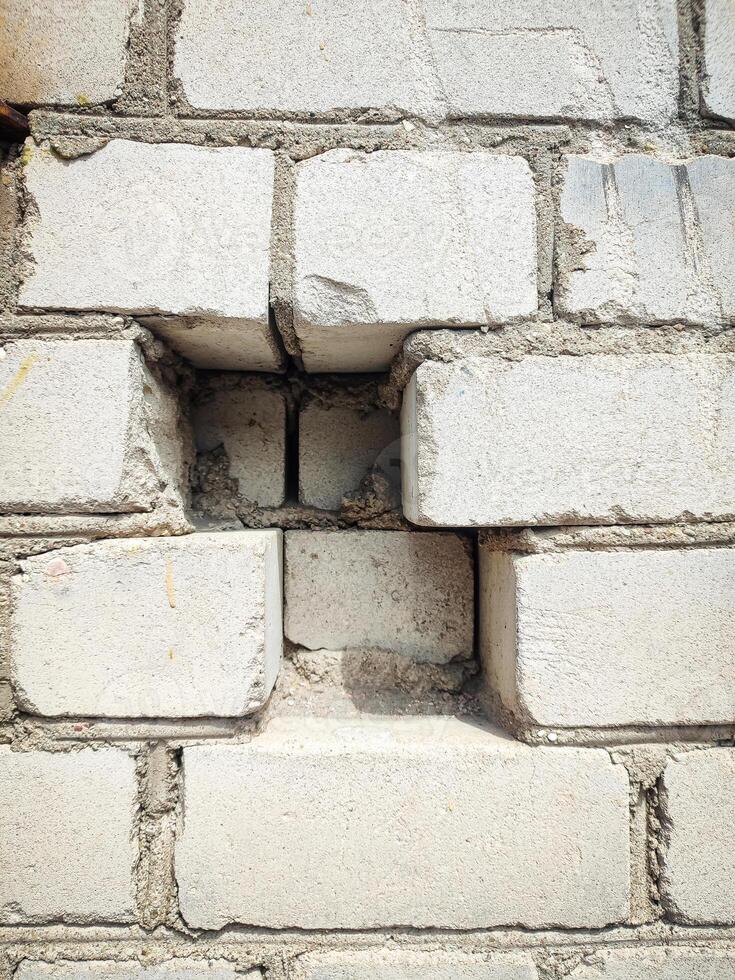 A close-up photo of a weathered white brick wall with a hole in the center