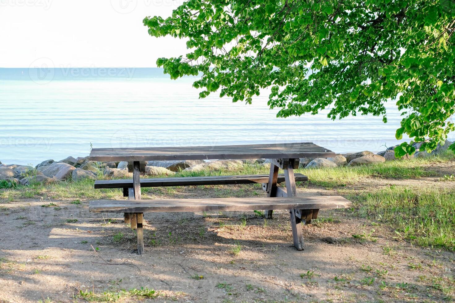 A wooden picnic table sits on the beach next to the water. photo