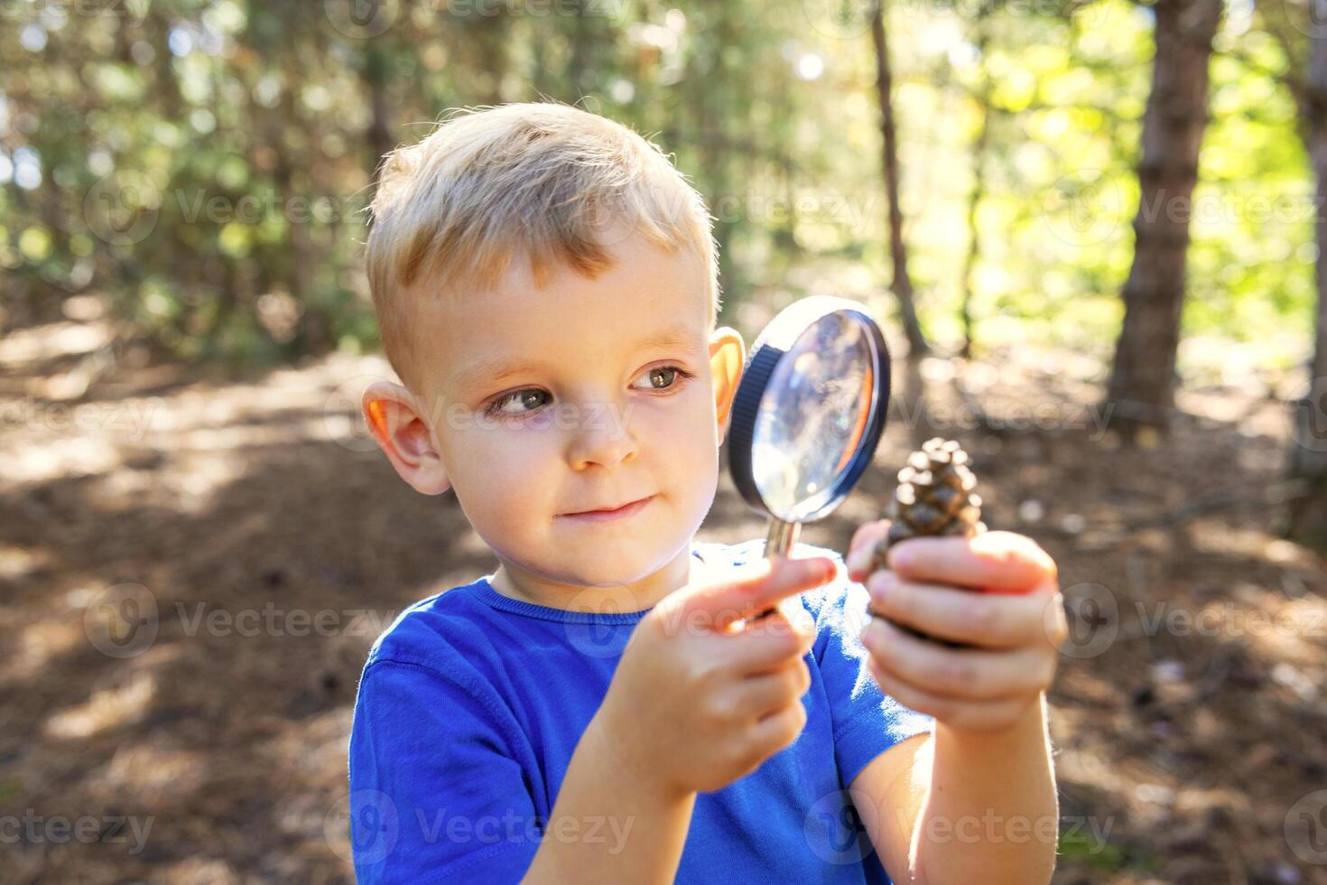 Curious boy is exploring nature with magnifying glass outdoors photo