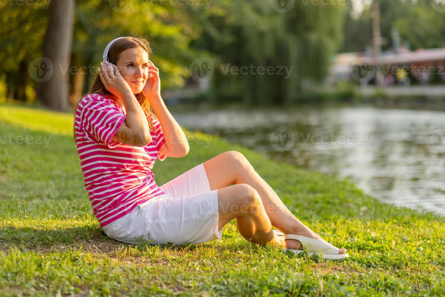 Relaxed woman sitting on the grass listening to music with headphones in a park photo