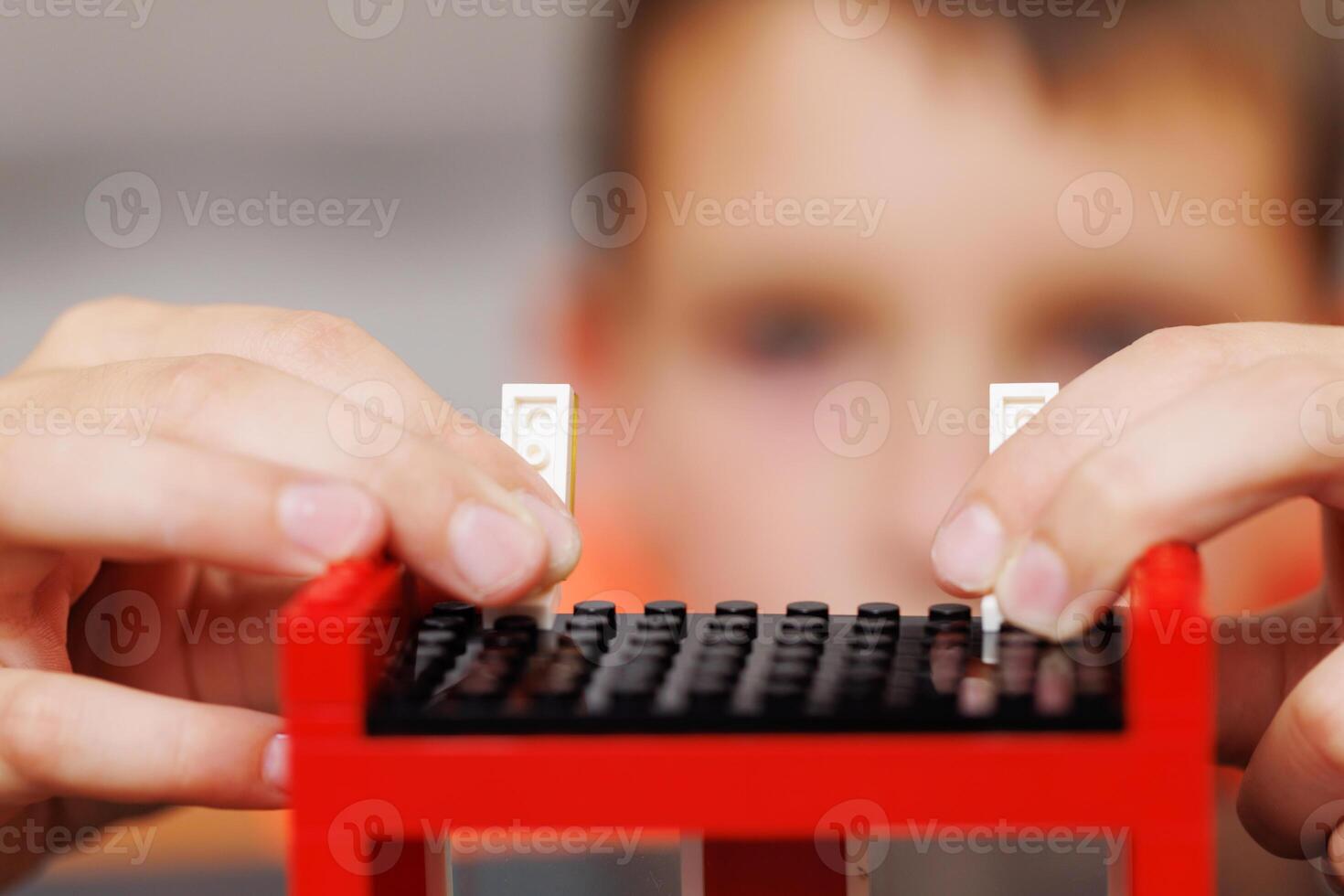 Child building a red toy structure with blocks on a table photo