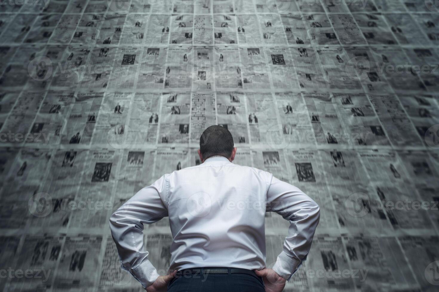 A man is standing in front of newspaper wall and reading the daily updates photo