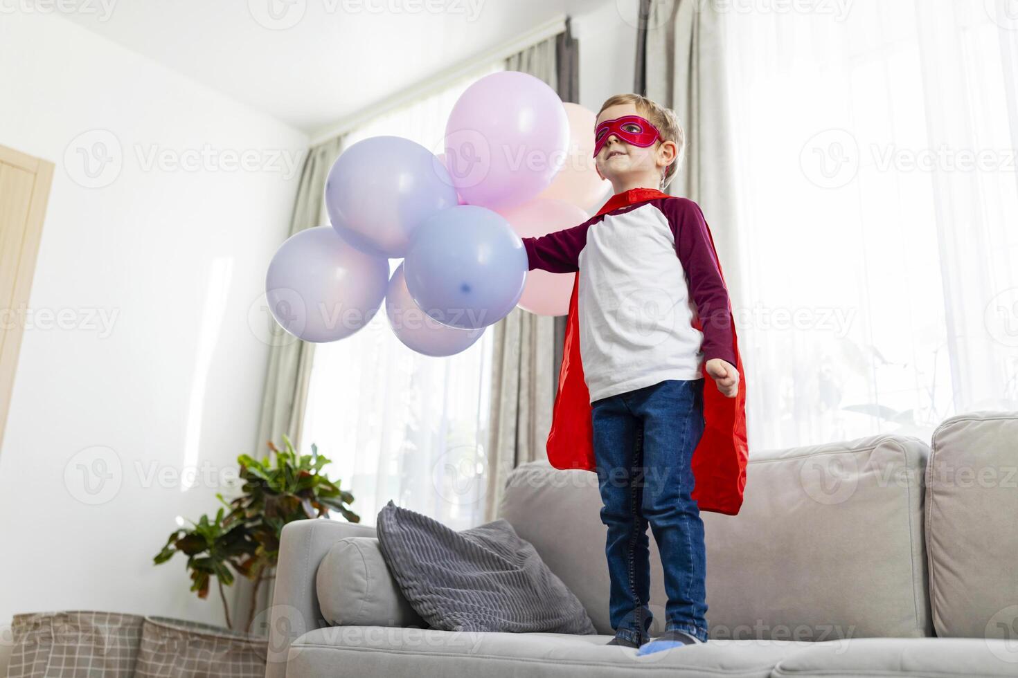 Boy in superhero costume with red cape and mask holding balloons photo