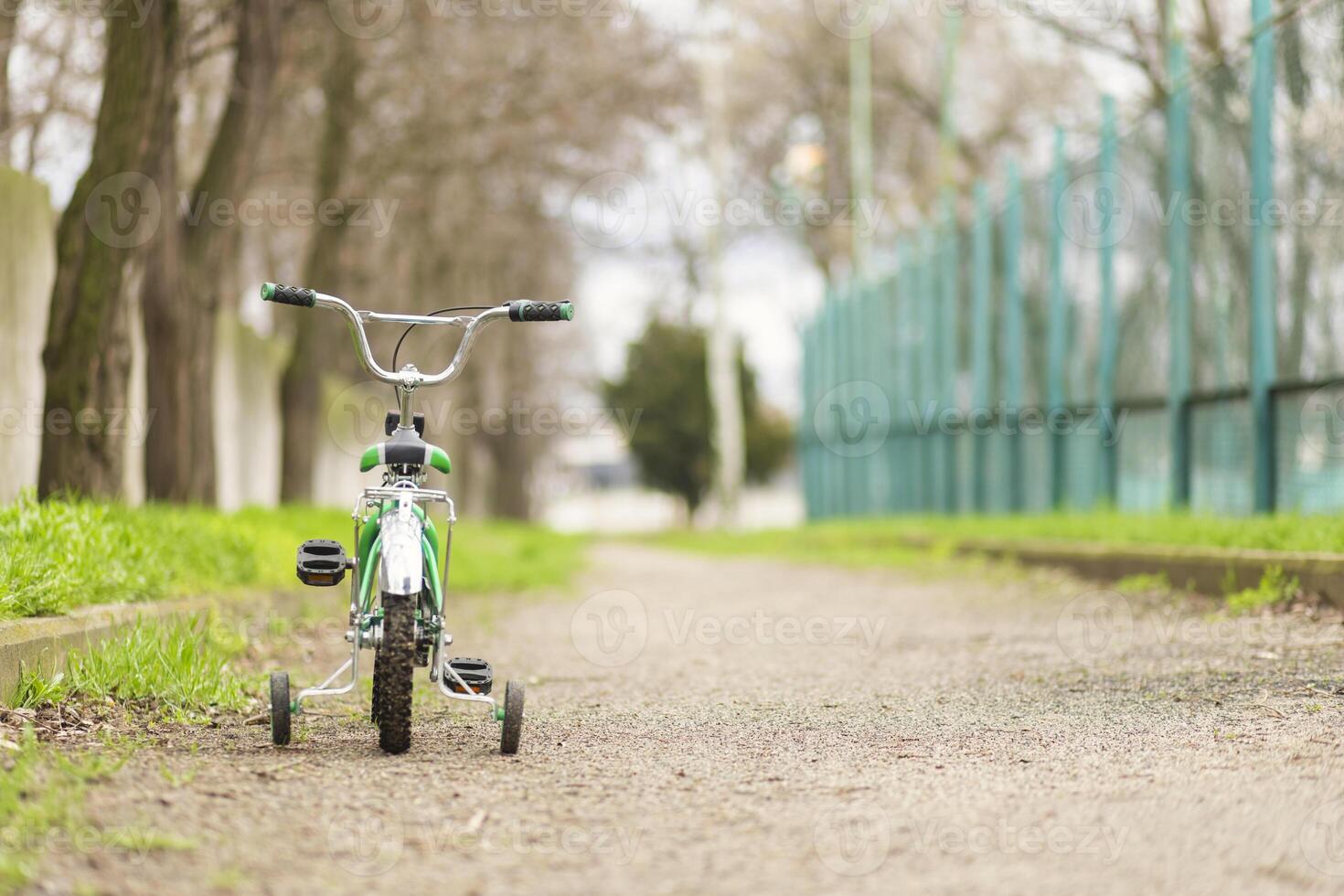 A green bicycle for children with additional wheels at road in park photo