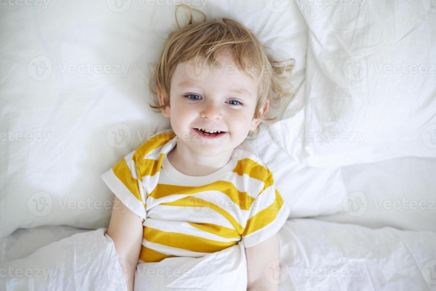 Top view of cheerful little boy in white bed early in the morning photo