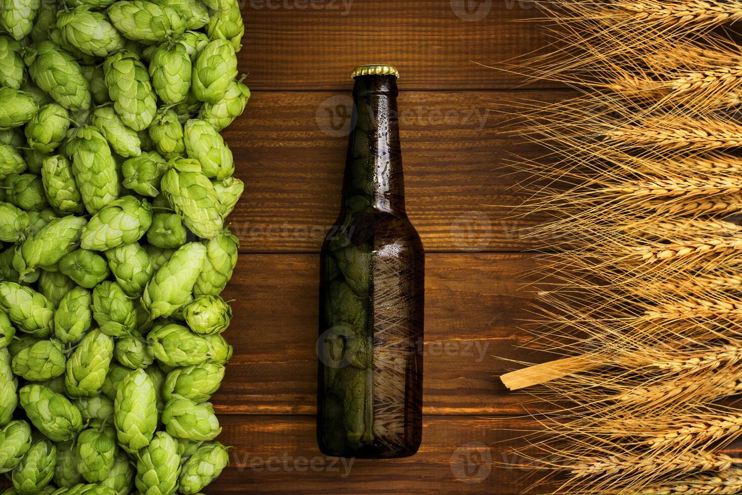 A bottle of beer on a wooden background with green hops and wheat ears photo