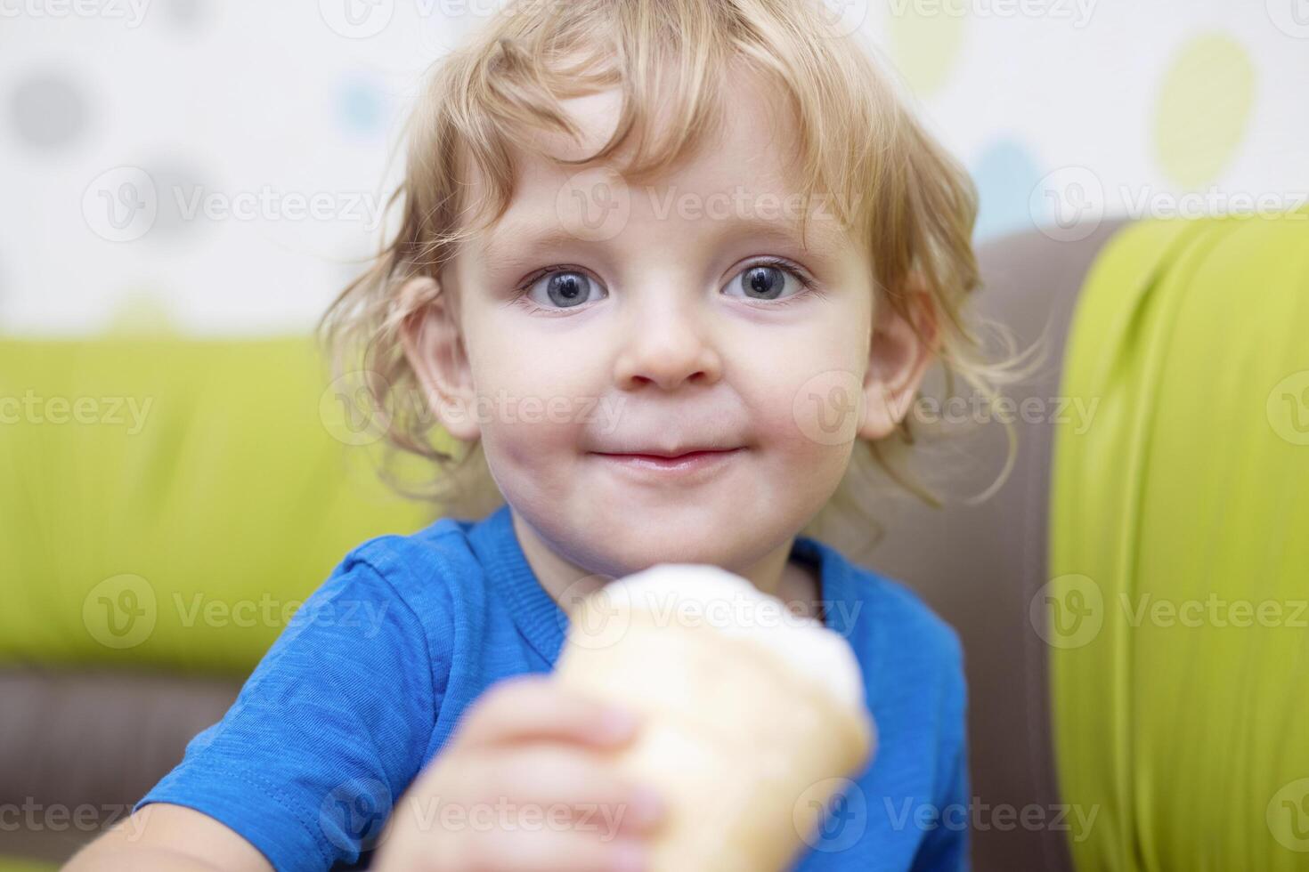 Happy little child in blue t-shirt eating ice cream at home photo