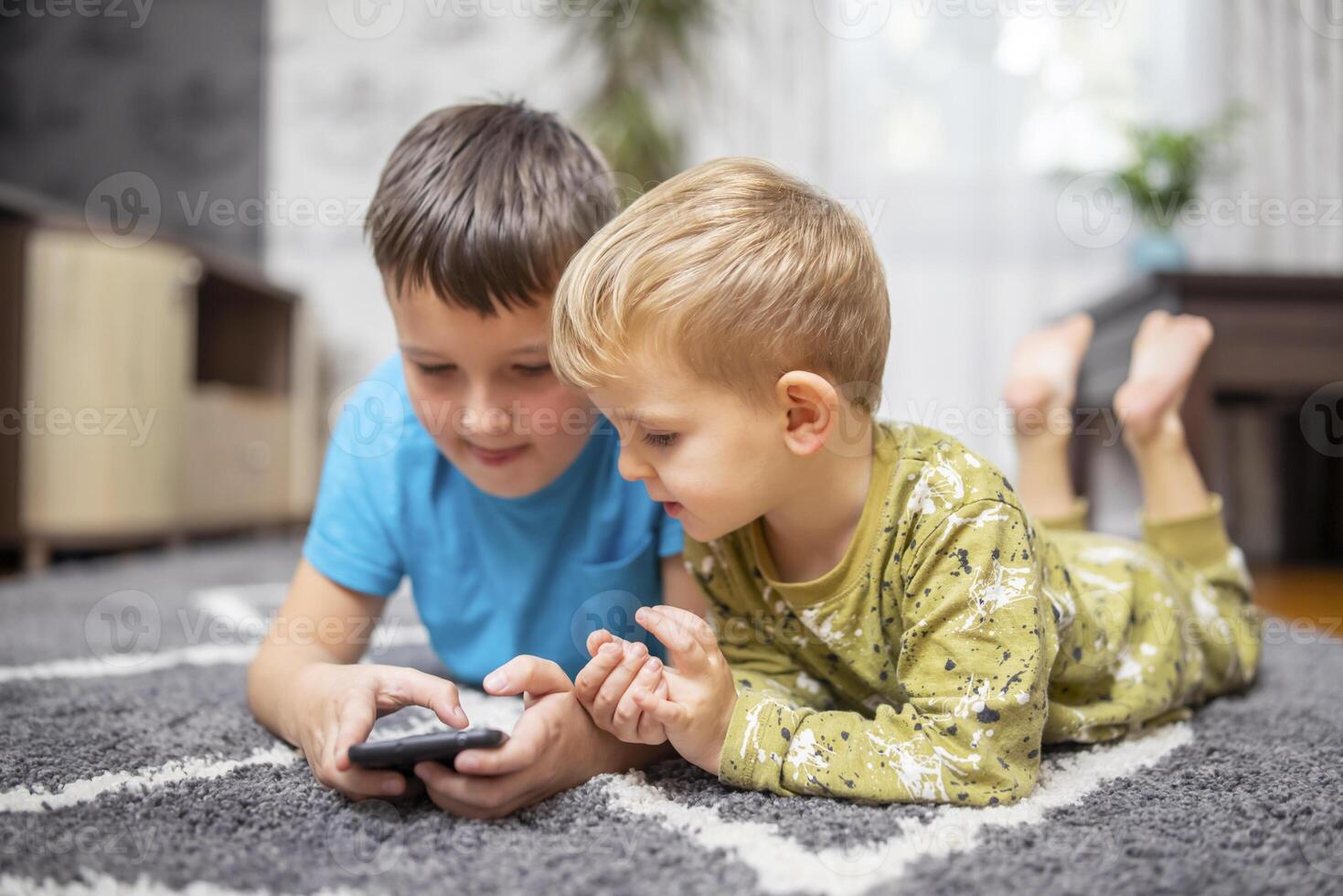 Two young boys lying on carpet using smartphone together photo