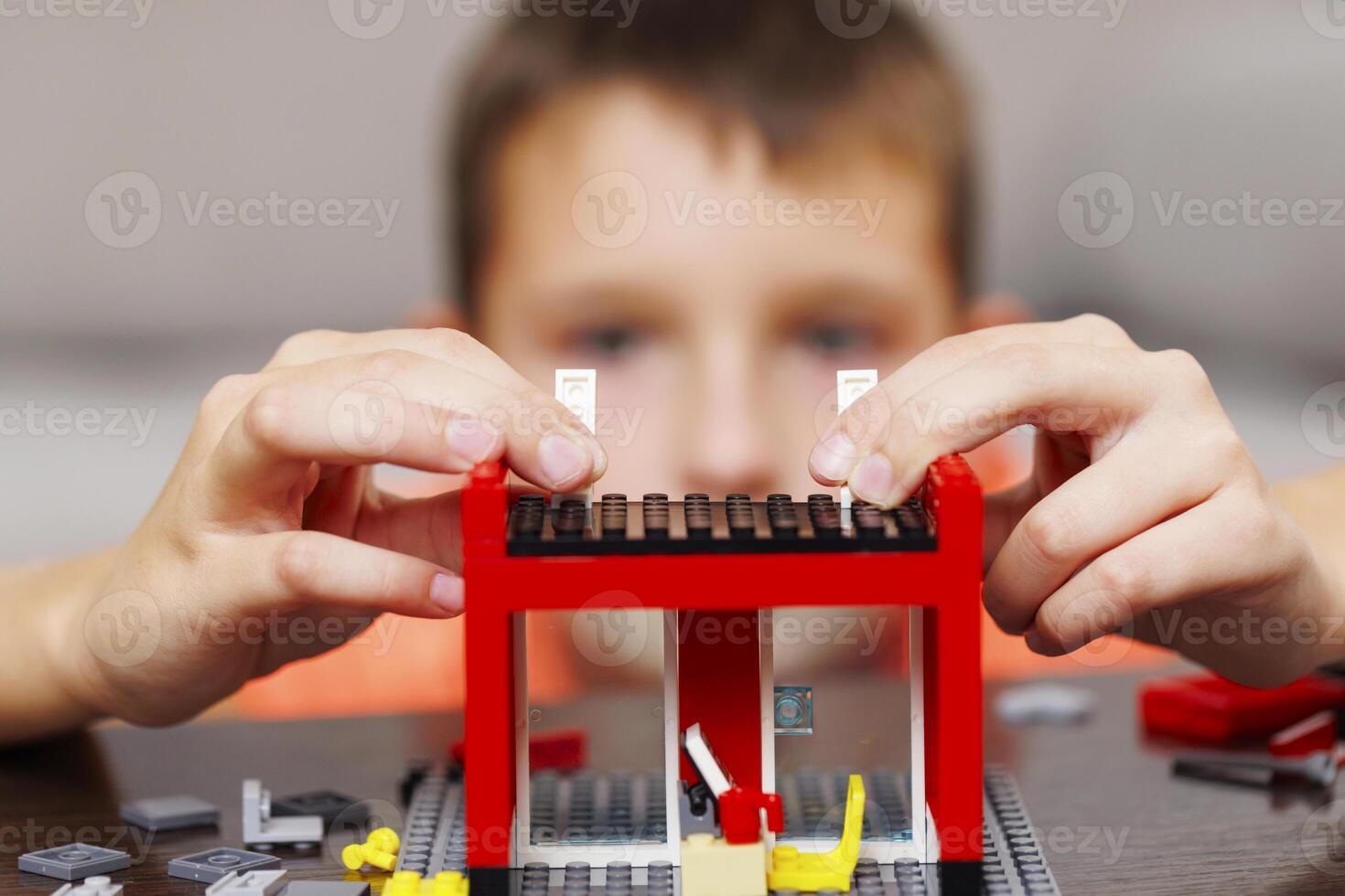 Child building a red toy structure with blocks on a table photo