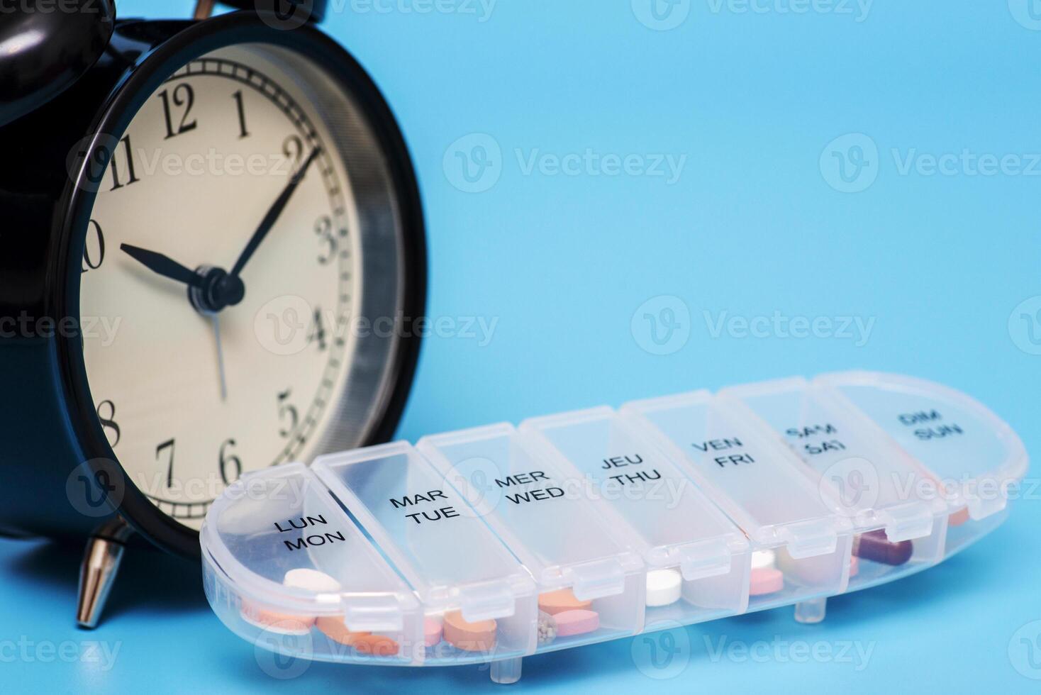 Plastic container with pills and black alarm clock on a blue background photo