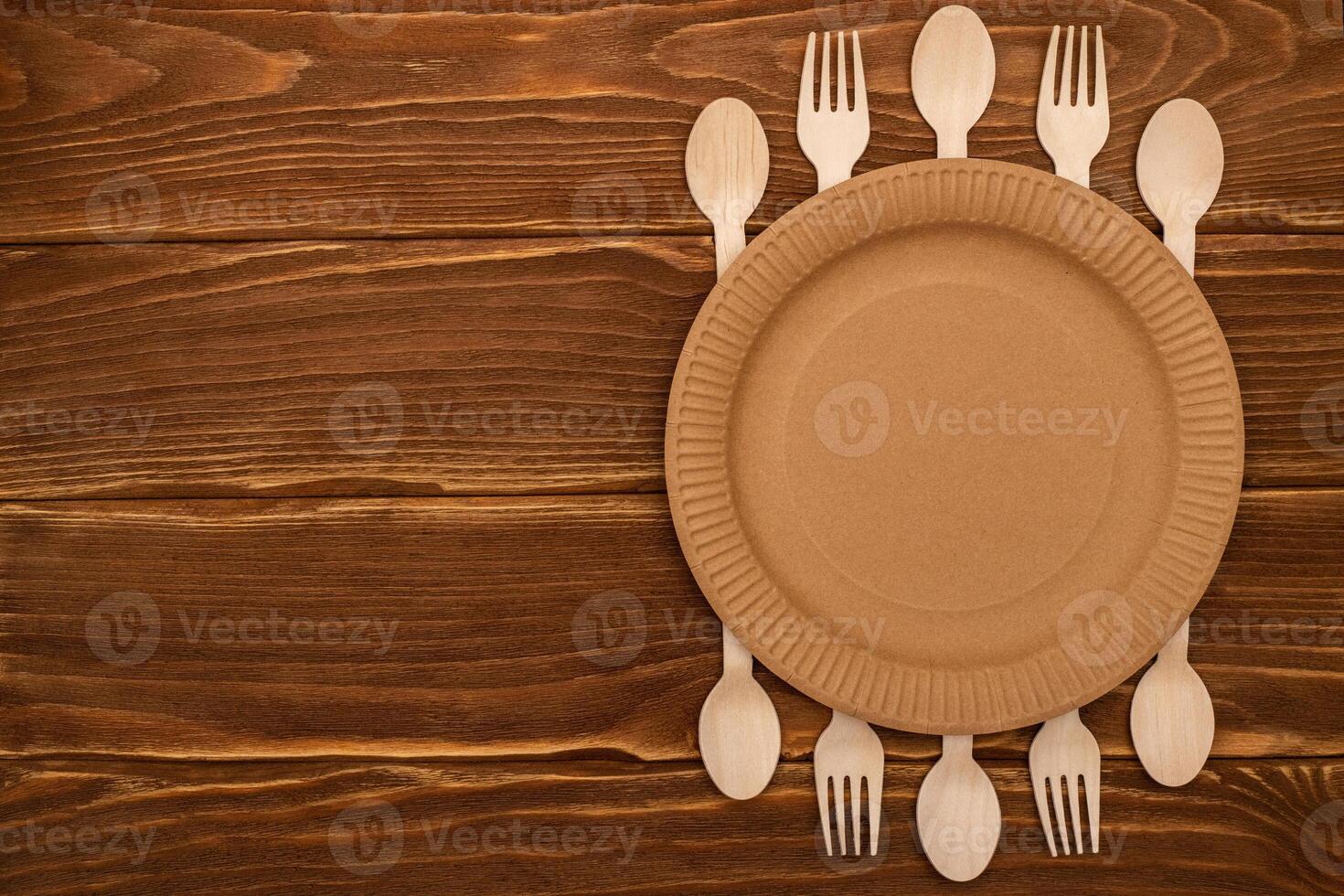 Wooden forks and spoons and paper plate on wooden background photo