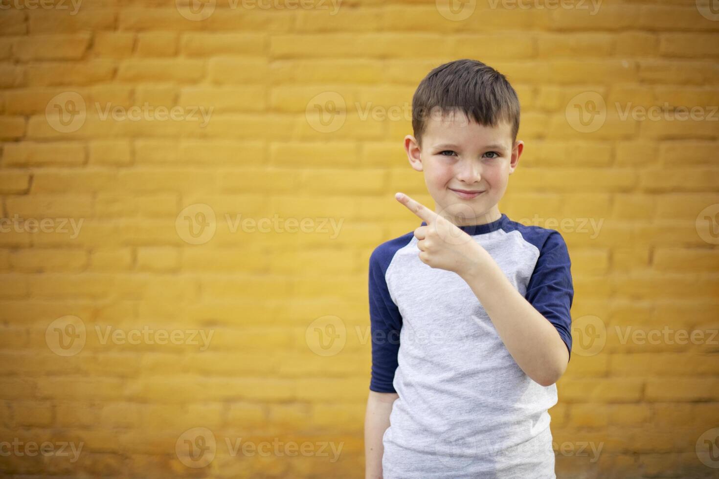 Smiling cute kid pointing with finger aside on yellow brick wall background photo